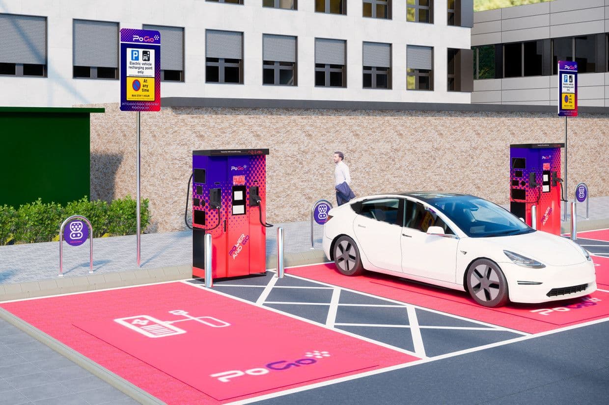 Aufladen eines Elektroautos an einer leuchtend roten und violetten PoGo-Ladestation auf einem Parkplatz, mit einem Gebäude im Hintergrund.
