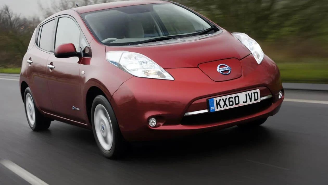 Red Nissan Leaf driving on a road with blurred greenery in the background, showcasing its sleek design and aerodynamic shape.