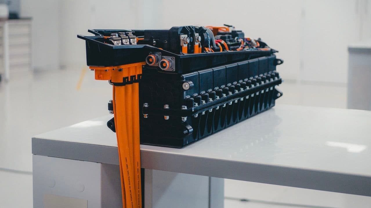 Close-up of an electric vehicle battery pack with orange cables on a white table in a bright room.