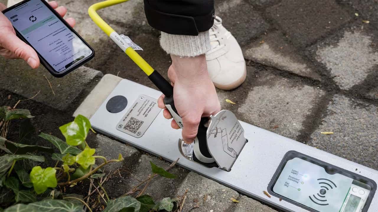 Persona utilizando una aplicación para smartphone para desbloquear un bordillo en una acera, rodeada de vegetación.