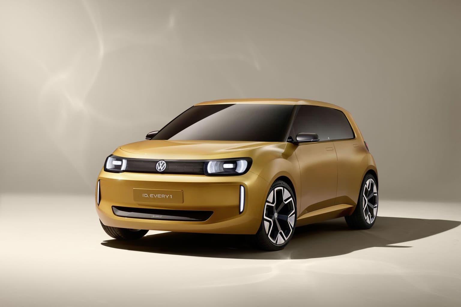 Un concept car Volkswagen elegante y dorado con un diseño moderno, con luces delanteras distintivas y ruedas elegantes, sobre un fondo neutro.