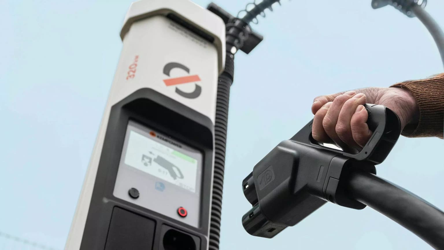 A person holds an electric vehicle charging plug near a Mobilize charging station with a display screen showing charging details.