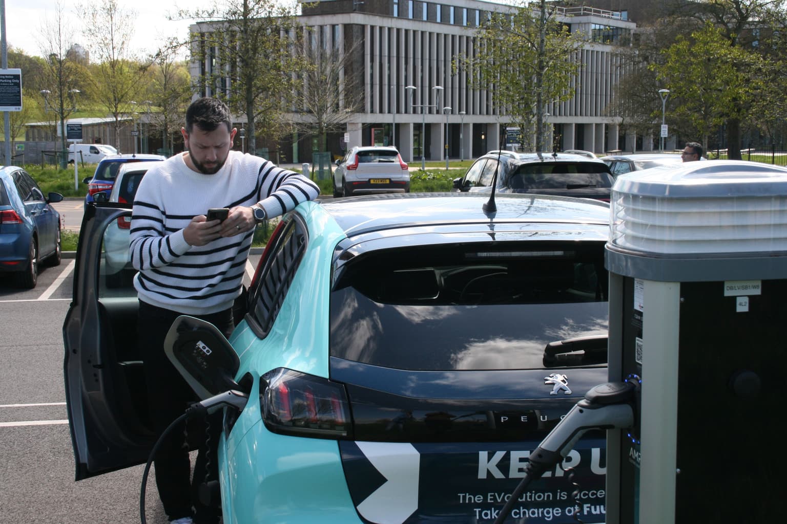 Man charging electric vehicle while on phone