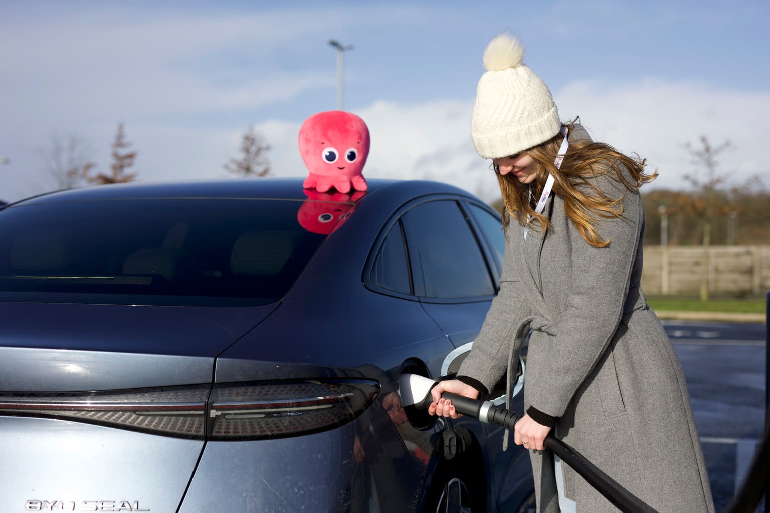 Woman holding EV cable next to BYD with Octopus plushie in background. Frau hält EV-Kabel neben BYD mit Oktopus-Plüschtier im Hintergrund