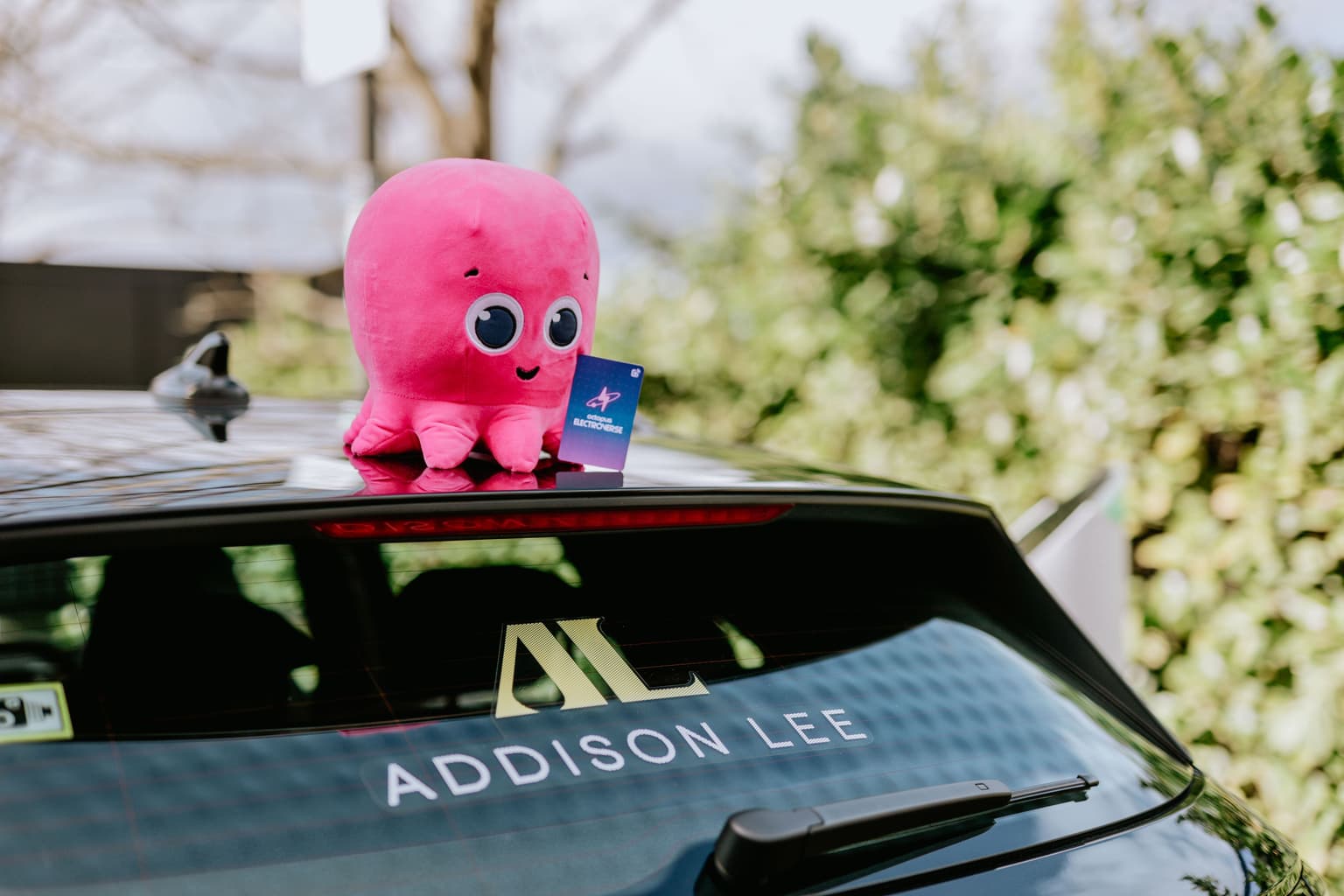 Octopus Energy mascot, Constantine, sits on top of Addsion Lee taxi holding an Octopus Electroverse charging card