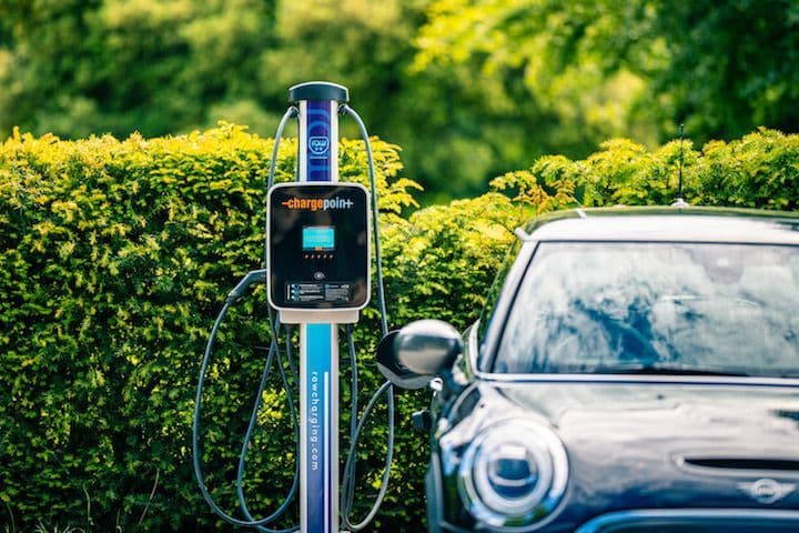 An einem sonnigen Tag wird ein Elektroauto an einer ChargePoint-Station aufgeladen, umgeben von grünem Laub.