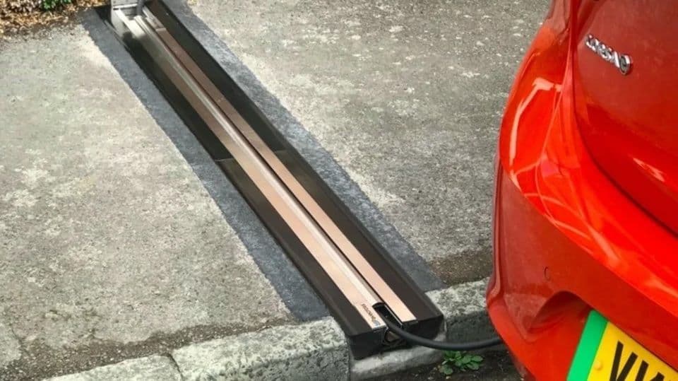 Coche rojo cargándose en una estación de recarga para vehículos eléctricos integrada en el pavimento junto a la acera.