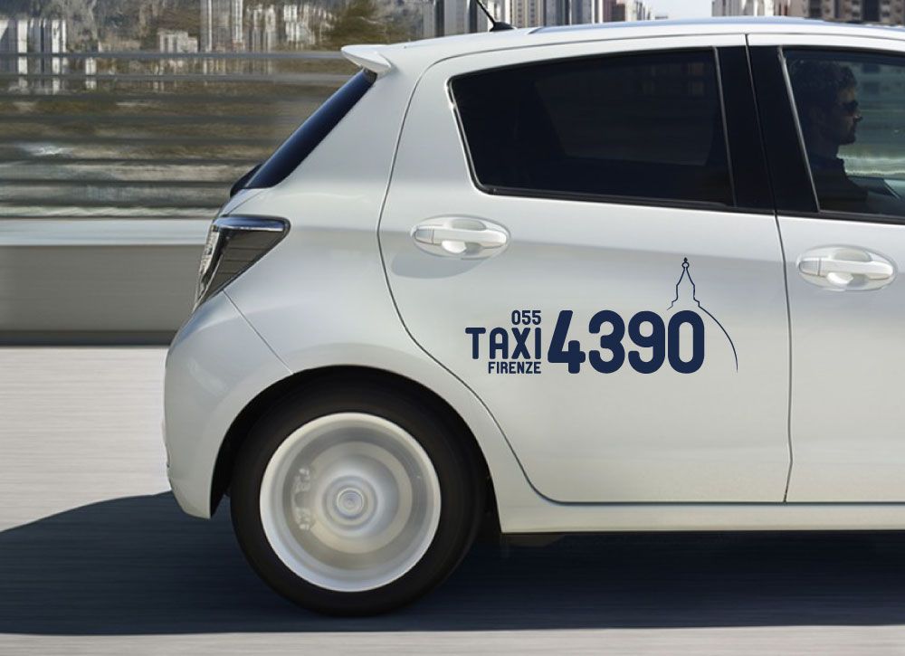 Taxi bianco con la scritta “055 Taxi Firenze 4390” e il profilo di una cupola sul lato, che circola su una strada.