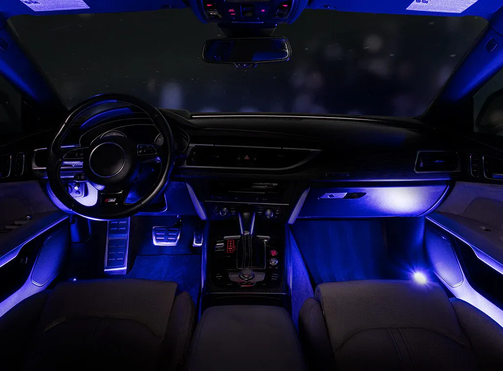 Interni dell'auto con cruscotto illuminato e illuminazione del vano piedi, dotati di volante, console centrale e luci d'ambiente blu.