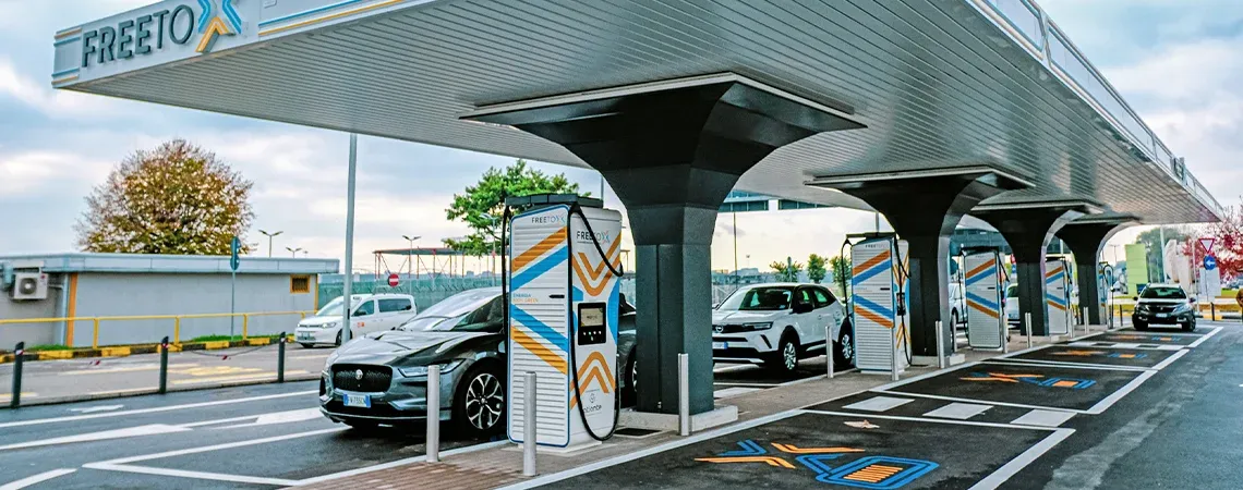 Veicoli elettrici in ricarica presso una colonnina Free to X con più punti di ricarica sotto un elegante tettoia.