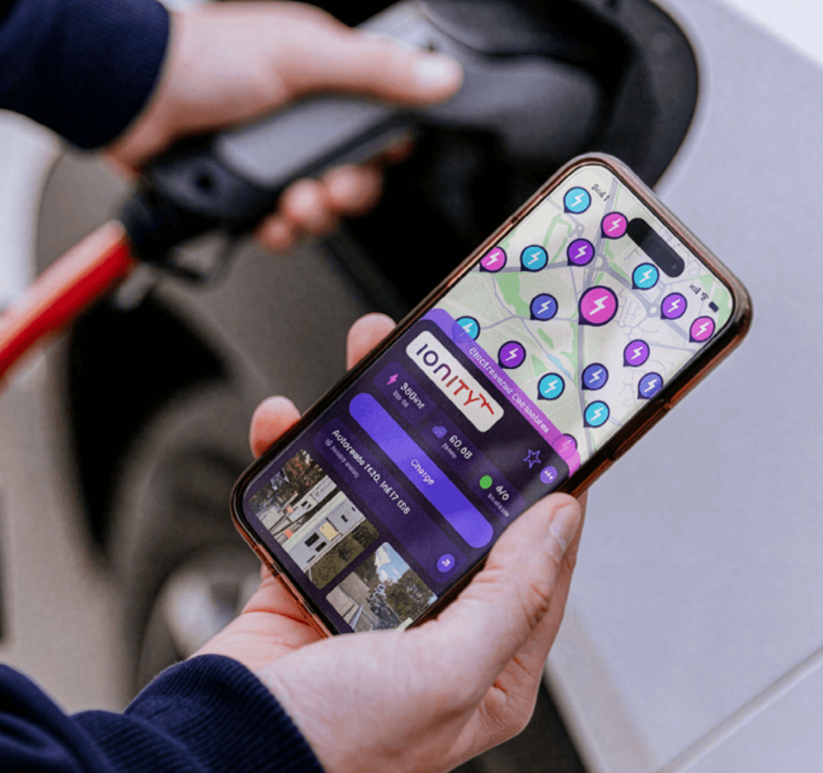A person uses a smartphone app to locate charging stations while plugging an electric vehicle into a charger.