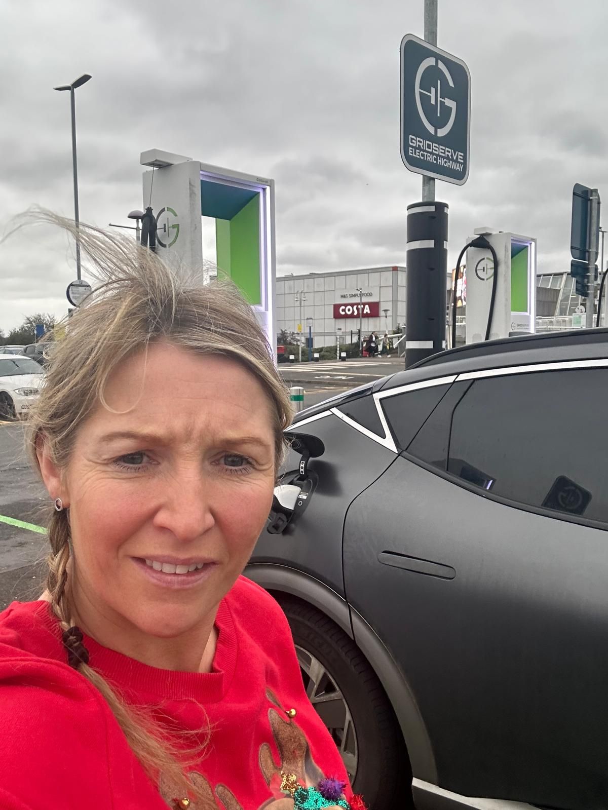 Amanda Armitage in a Christmas jumper at a EV charger. Amanda Armitage con un jersey navideño en un cargador de vehículos eléctricos. Amanda Armitage con un maglione natalizio presso una stazione di ricarica per veicoli elettrici. Amanda Armitage com uma camisola de Natal num carregador de veículos elétricos. Amanda Armitage in einem Weihnachtspullover an einer Ladestation für Elektrofahrzeuge. Amanda Armitage portant un pull de Noël près d'une borne de recharge pour véhicules électriques.