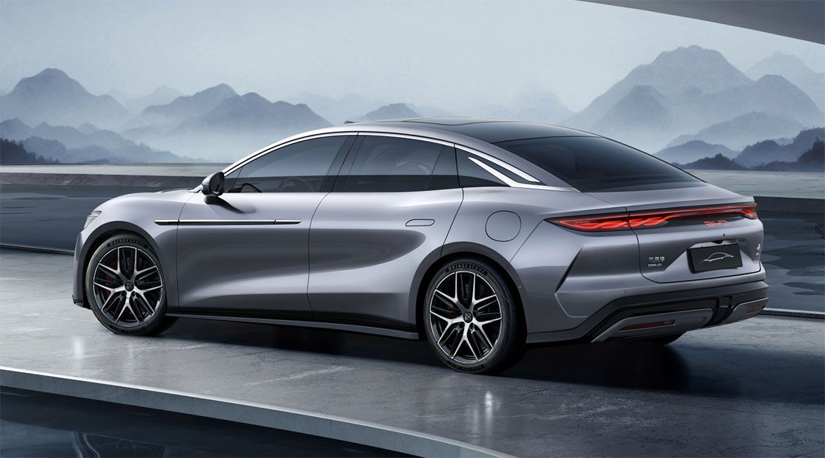 Elegante sedán plateado con un diseño moderno, estacionado sobre una superficie de concreto, con montañas en el fondo brumoso.