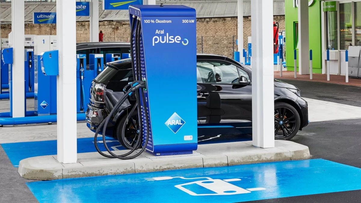 Electric vehicle charging at an Aral Pulse station, featuring a blue charger labeled "100% Ökostrom 300 kW," with a blue parking area.