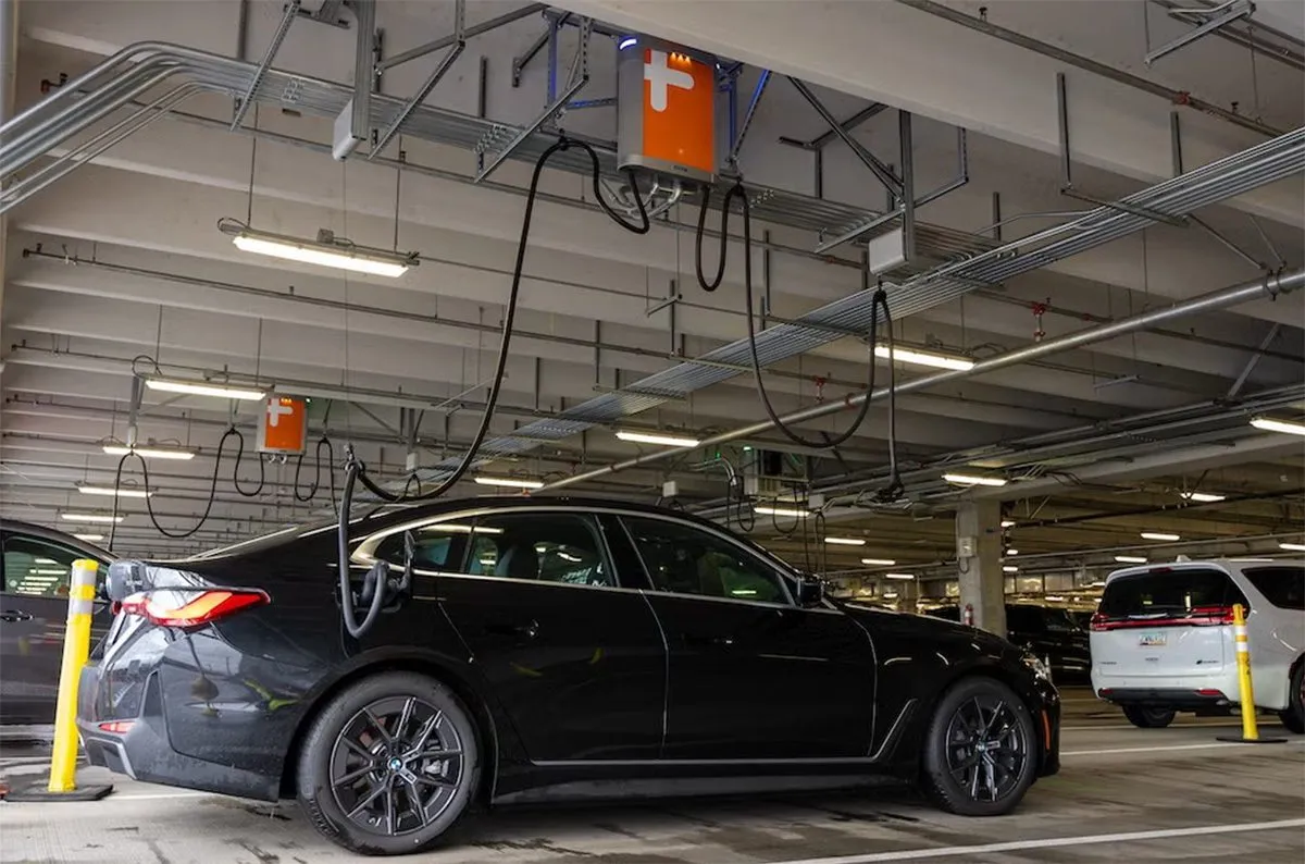 Recharge d'une voiture électrique à une borne située dans un parking couvert, avec des câbles suspendus au plafond.