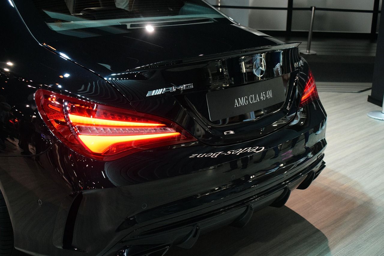 Rear view of a black Mercedes AMG CLA 45 4M with illuminated taillights in a showroom setting.