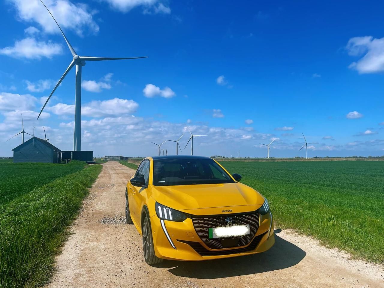 Yellow car in front of field with wind turbines. Coche amarillo delante de un campo con aerogeneradores. Auto gialla davanti a un campo con turbine eoliche. Carro amarelo em frente ao campo com aerogeradores. Gelbes Auto vor einem Feld mit Windrädern. Voiture jaune devant un champ avec des éoliennes.