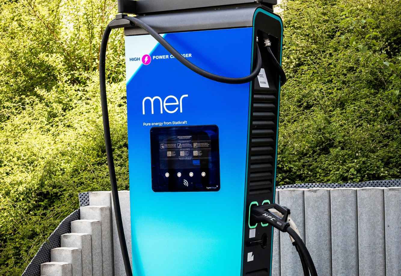 Elektrofahrzeug-Ladestation mit „mer“-Branding, in blau-schwarzem Design, vor einem grünen Hintergrund.