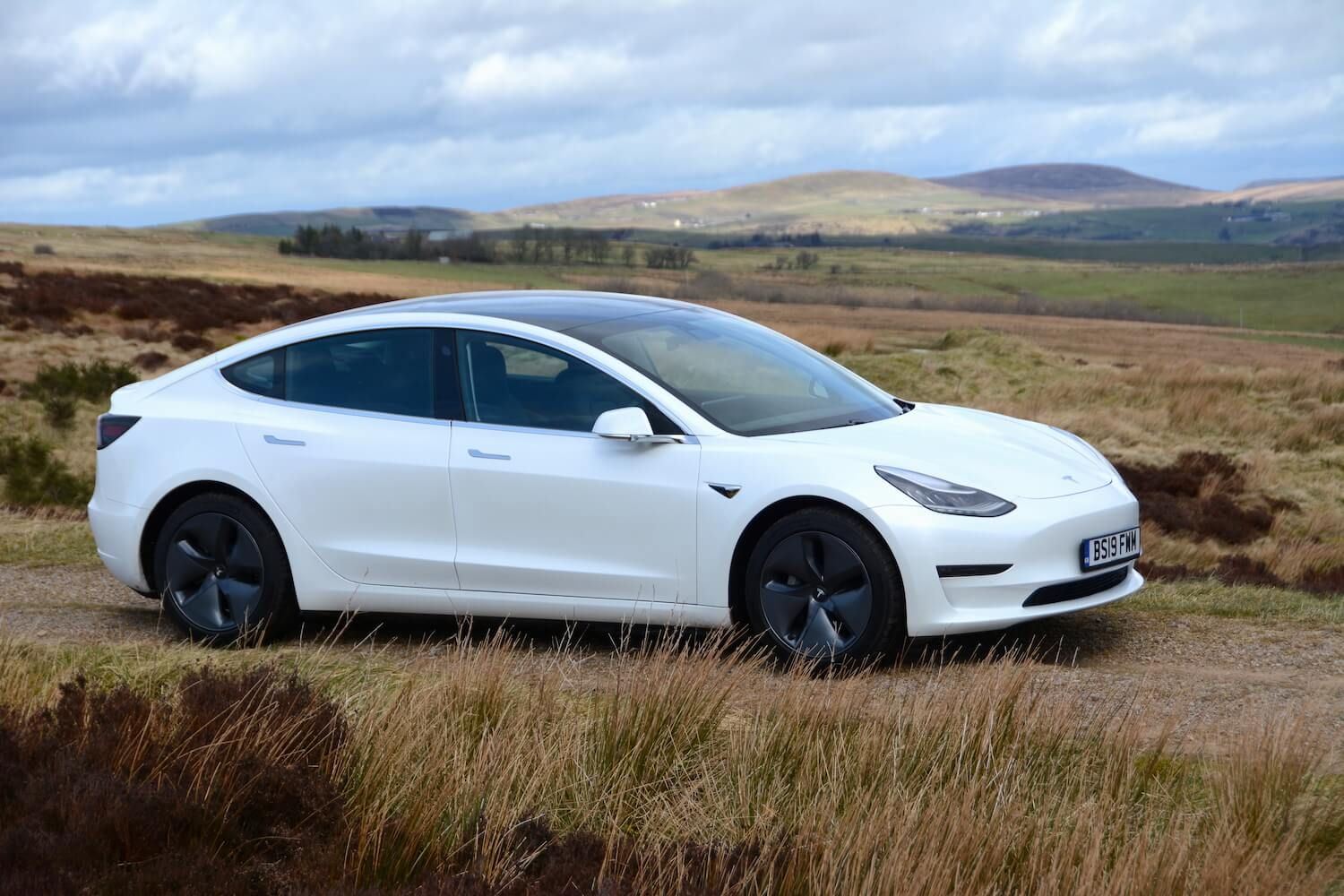 Un'auto elettrica Tesla Model 3 Long Range bianca che attraversa la campagna