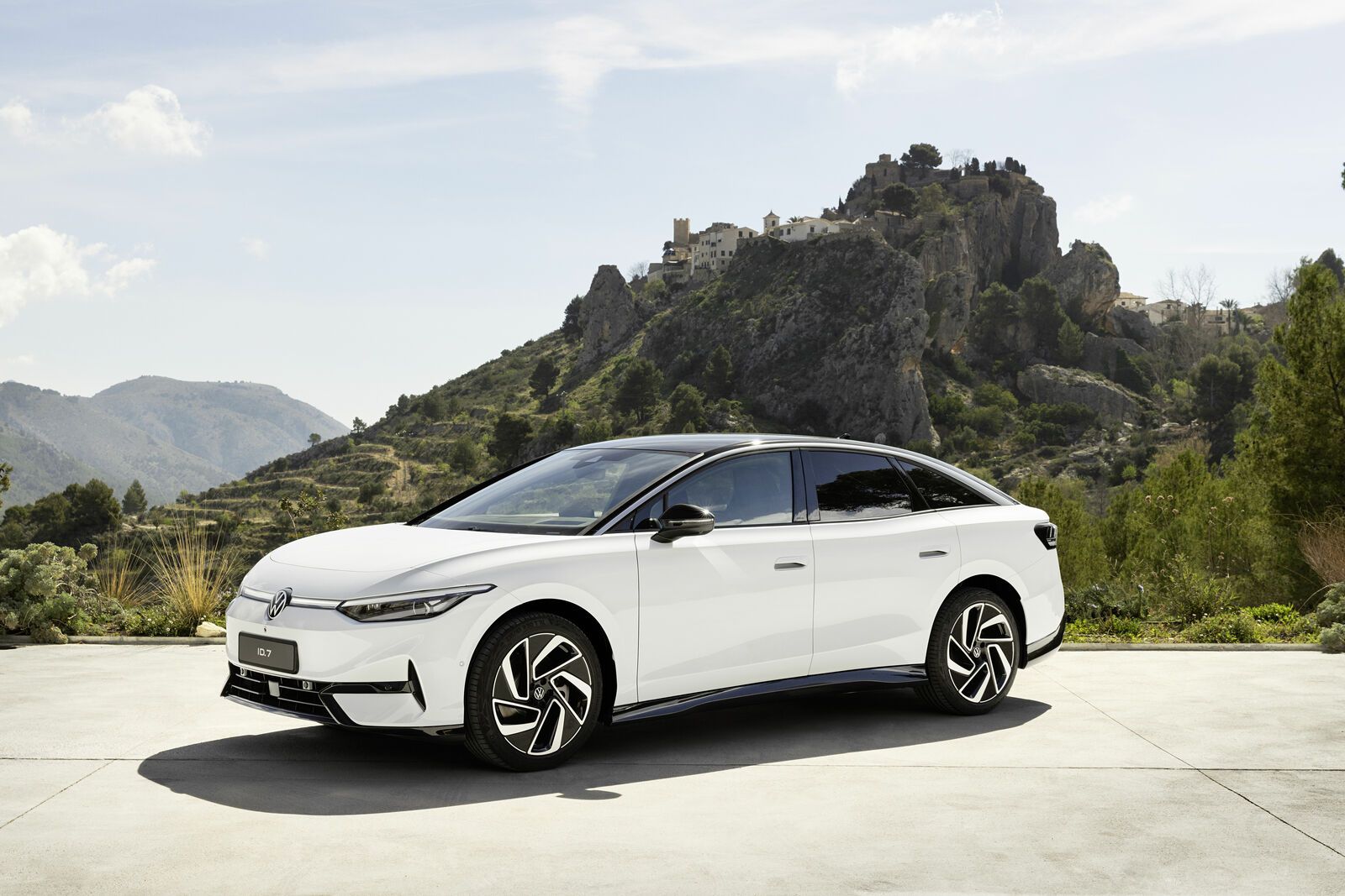 Un'auto elettrica Volkswagen ID.7 Pro bianca, sullo sfondo di una montagna alberata
