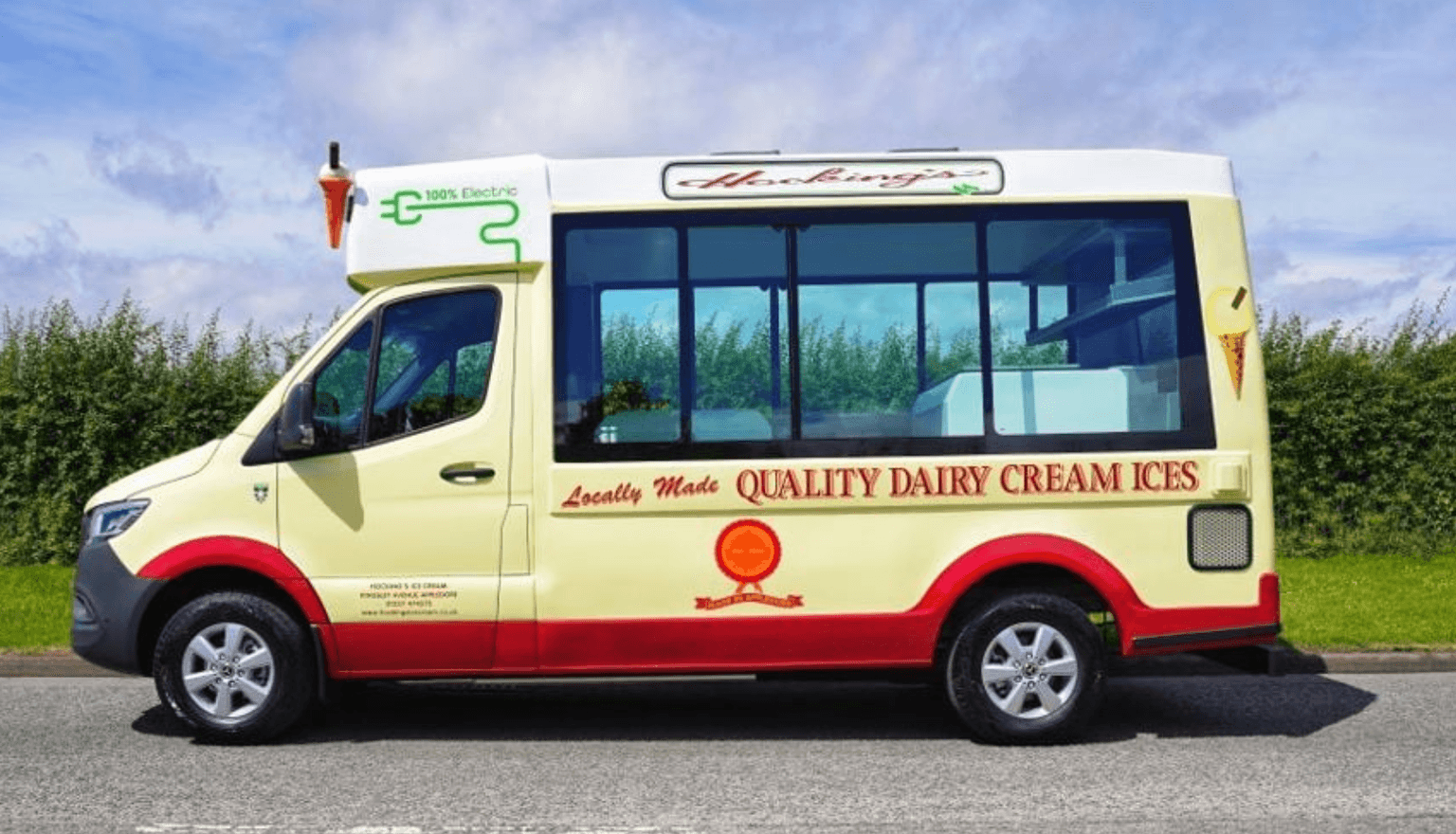 A cream and red electric ice cream van parked on the road, with "Locally Made Quality Dairy Cream Ices" written on its side.