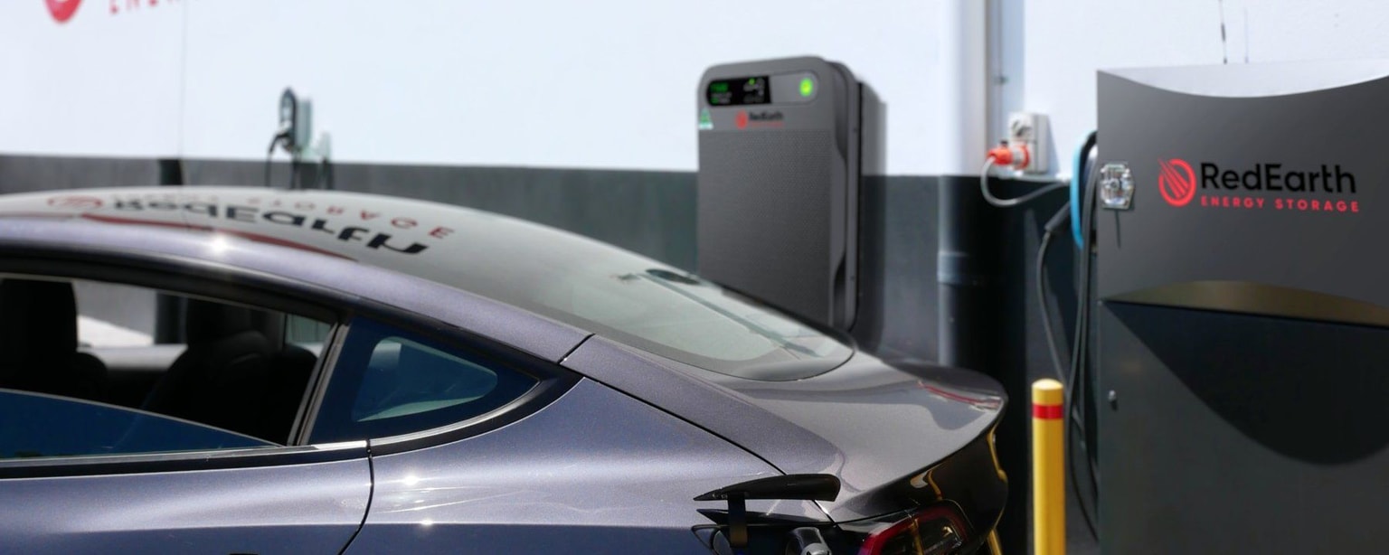 Auto elettrica in ricarica presso una stazione di stoccaggio di energia RedEarth, con un elegante veicolo grigio collegato a un'unità di ricarica.