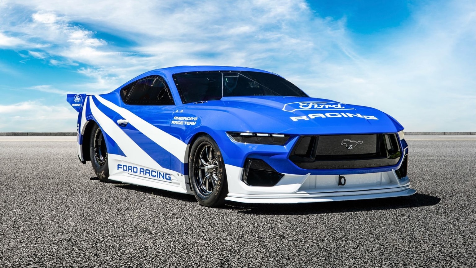 Blue Ford electric racing car with white accents parked on an asphalt road under a clear sky.