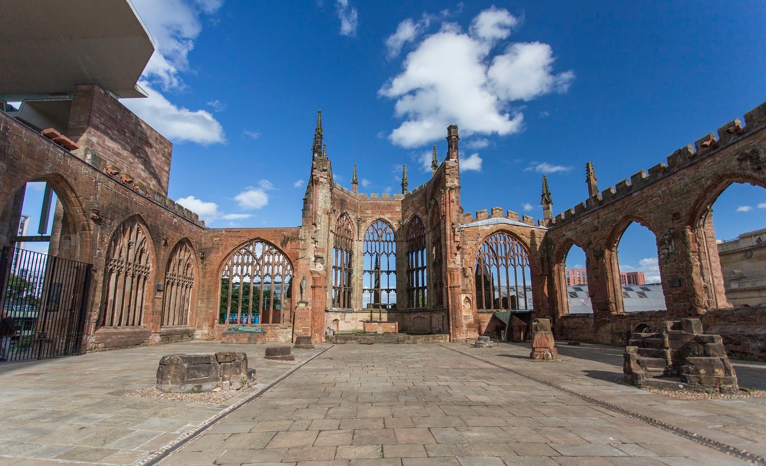 Ruins of a historic cathedral with arched windows and stone walls under a blue sky with clouds.