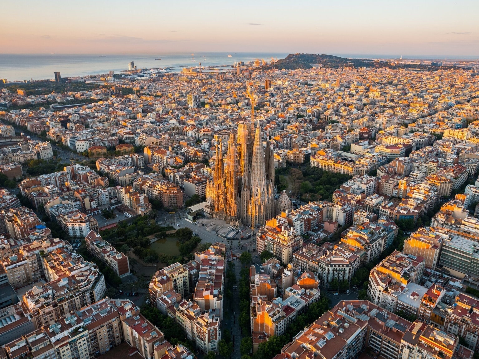 Vista aérea de Barcelona al atardecer, destacando la Sagrada Familia rodeada de edificios y calles densamente pobladas.