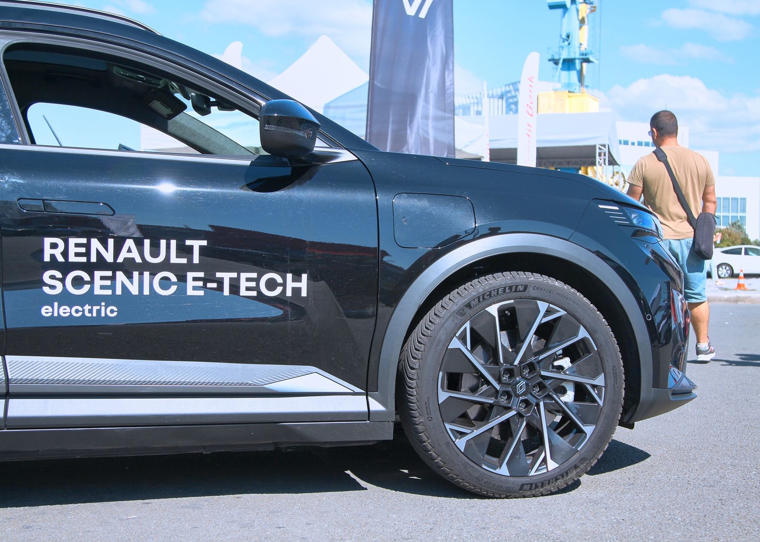Close-up of a black Renault Scenic E-Tech electric car with label on the side and stylish alloy wheels, parked outdoors.