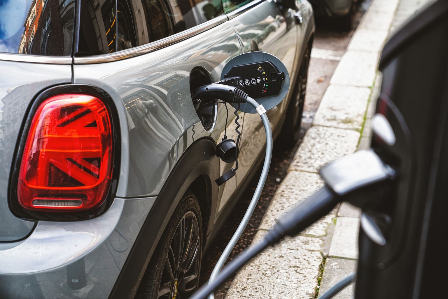 Electric car charging on a city street with a visible charging cable and connector plugged into the vehicle's side.