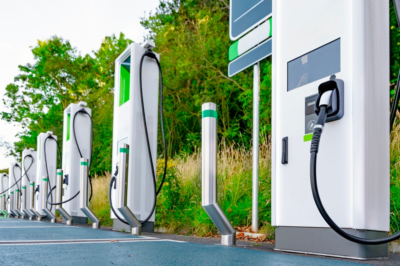 Borne de recharge pour véhicules électriques avec plusieurs unités de recharge blanches alignées près de la végétation verte.