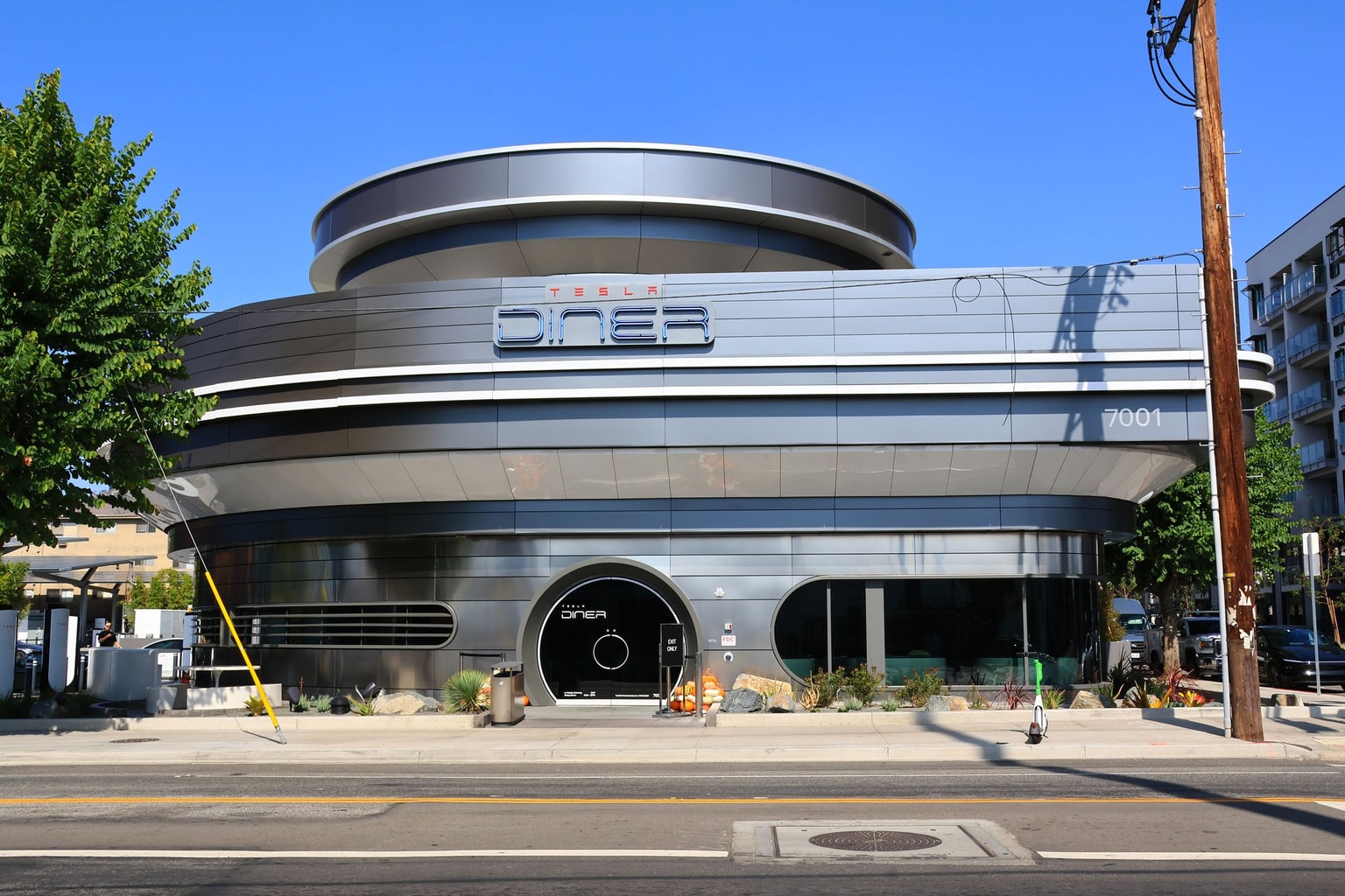 Modern silver cylindrical building labeled "Diner" with large windows, trees, and a scooter parked outside on a sunny day.