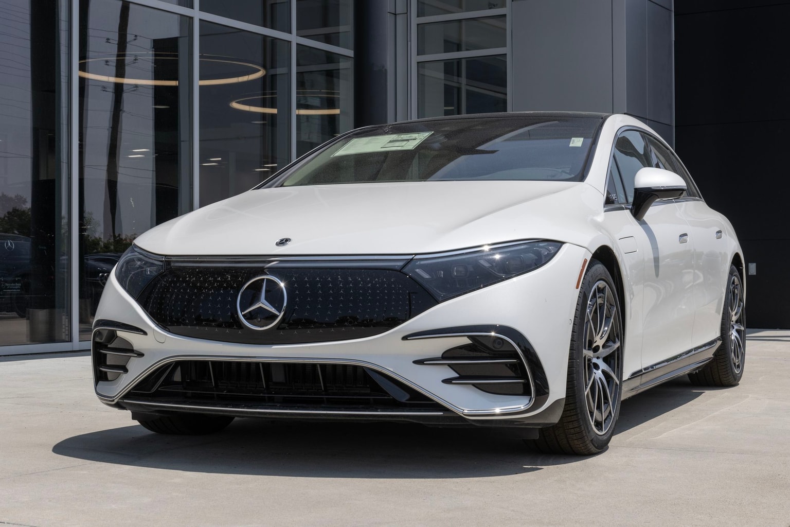 White Mercedes-Benz electric sedan parked in front of a modern building with large windows.