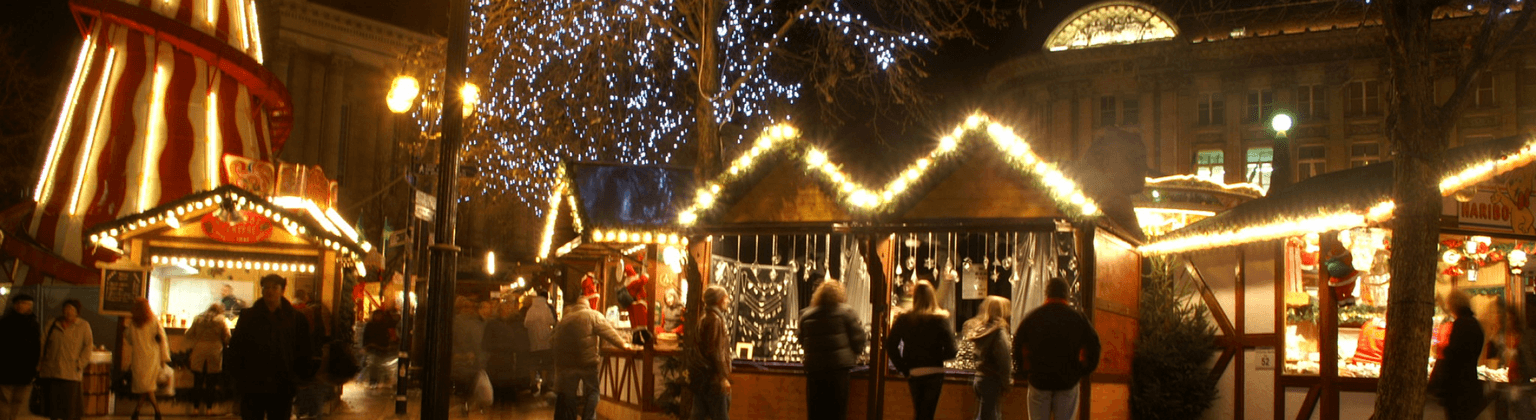 Festivo mercatino di Natale di Birmingham di notte, con bancarelle illuminate, luci scintillanti e gente che curiosa in un'atmosfera vivace e calda.