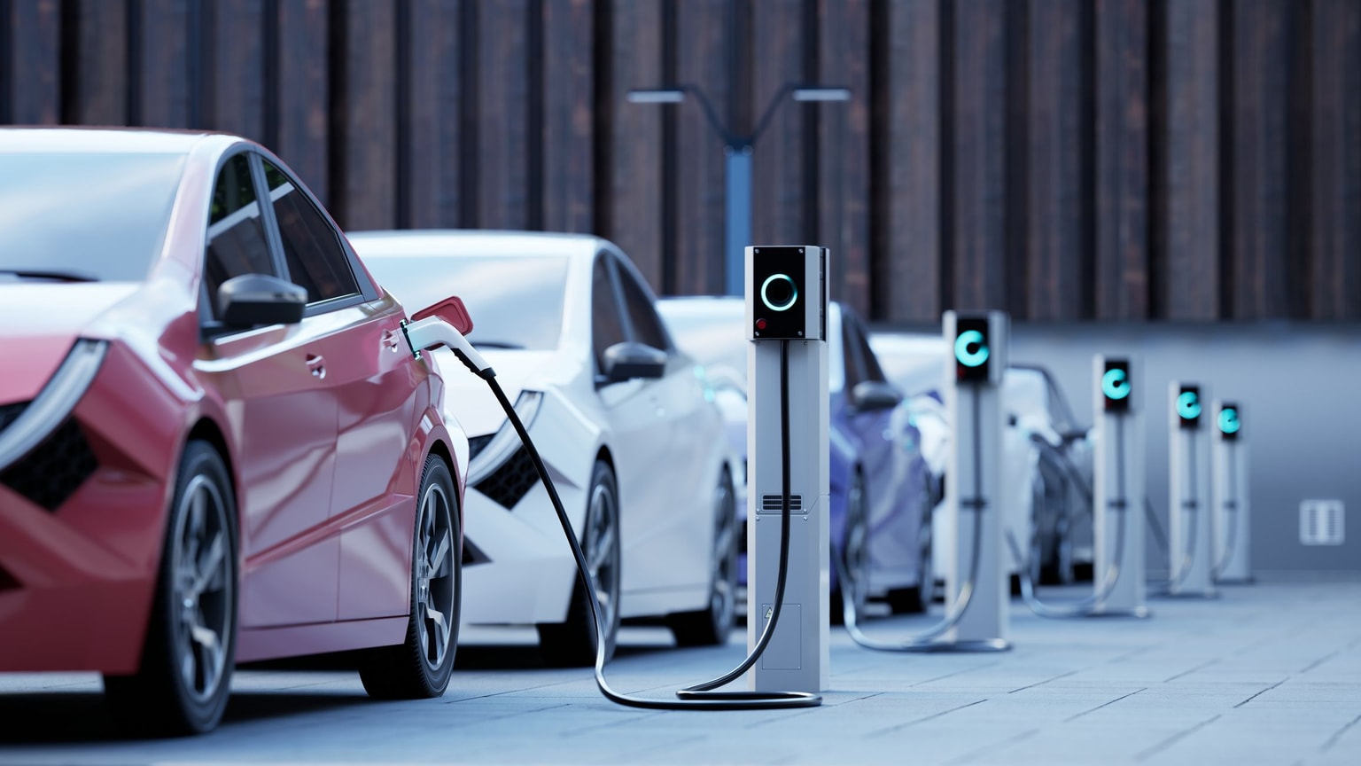 Row of electric cars charging at modern charging stations in an outdoor setting, with a focus on the red car in front.