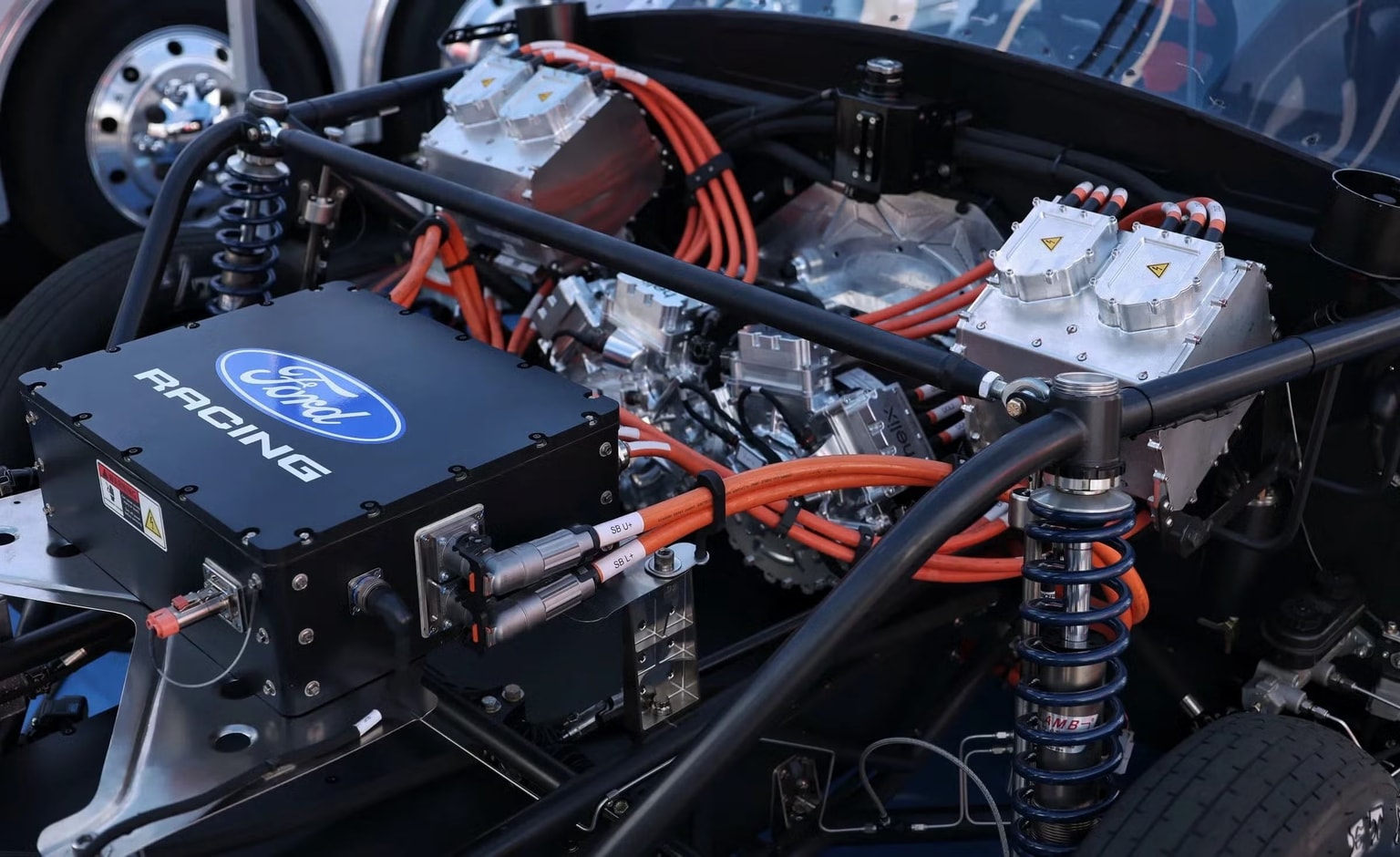 Close-up of a Ford Racing electric motor setup, featuring orange cables, metal components, and suspension springs.