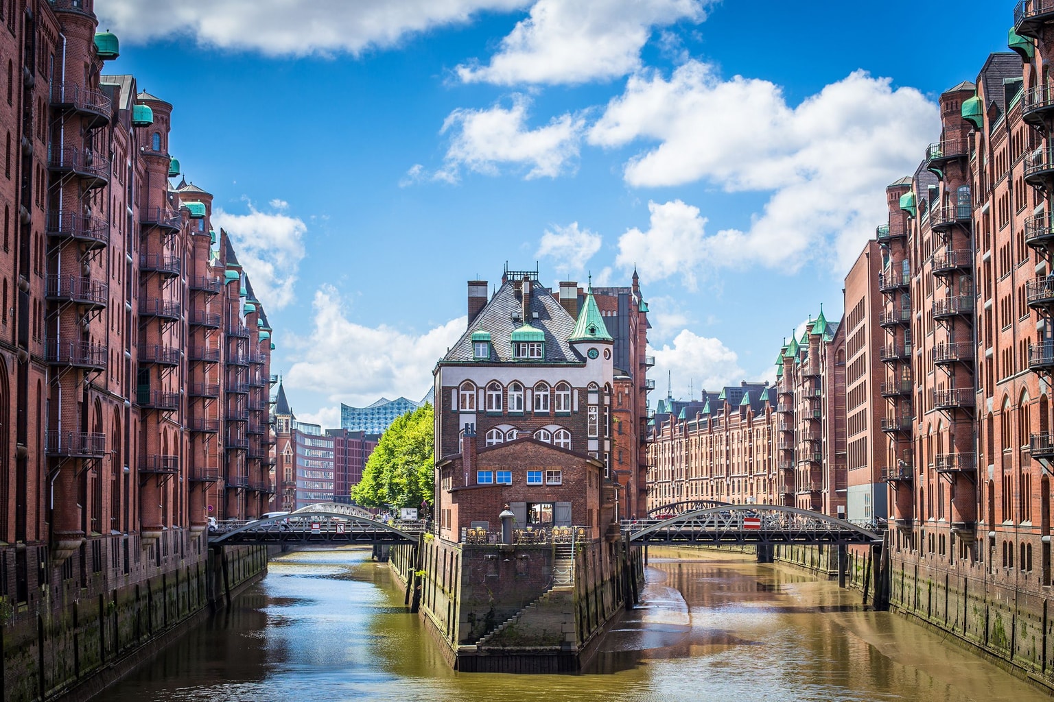 Historische Backsteingebäude säumen einen Kanal in der Hamburger Speicherstadt, mit einem zentralen Gebäude und blauem Himmel darüber.