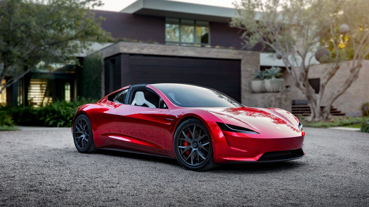 Ein Konzeptbild eines roten Tesla Roadsters, das Auto steht auf einer Kiesauffahrt, im Hintergrund ein modernes Haus und Bäume.