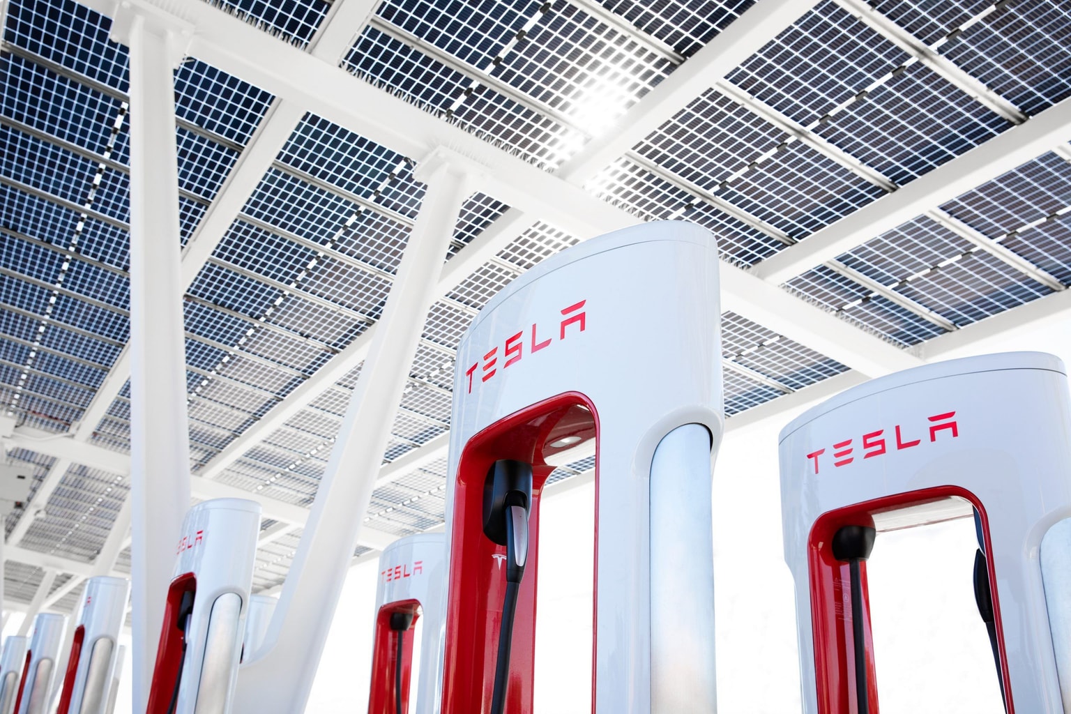Stations de recharge Tesla sous un auvent de panneaux solaires, vues sous un angle bas, mettant l'accent sur la technologie de l'énergie propre.
