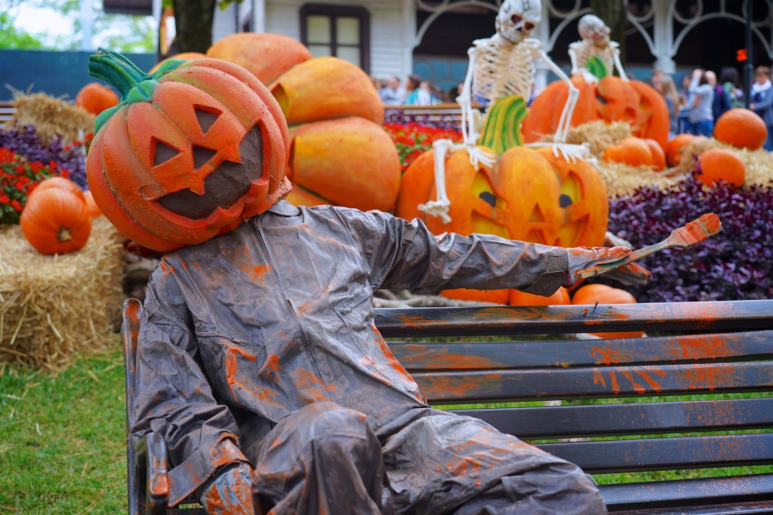 Gardaland Park. Persona vestita con un costume da testa di zucca seduta su una panchina, circondata da grandi zucche e decorazioni di Halloween, tra cui scheletri.