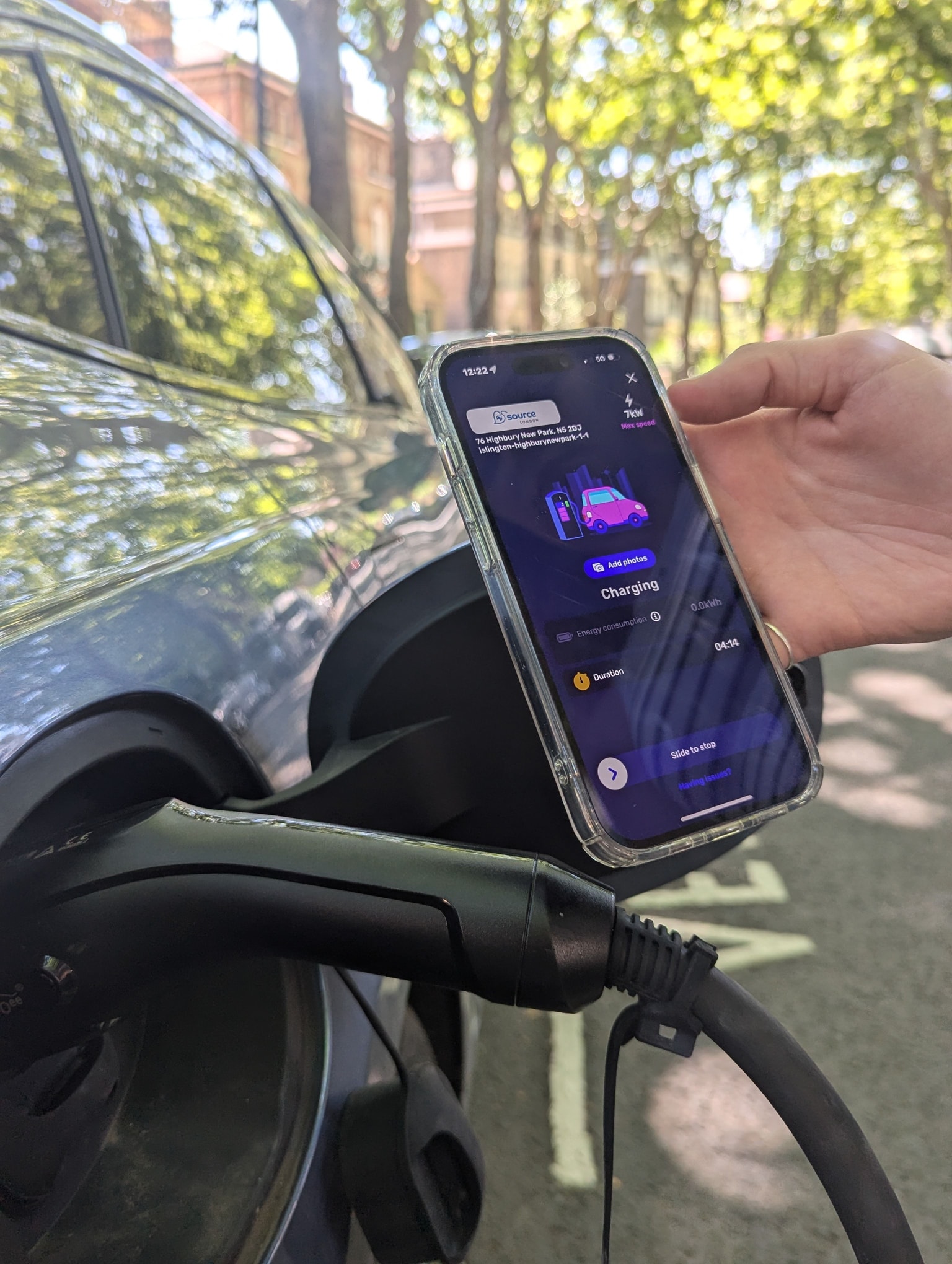 Hand holding a smartphone displaying the Electroverse app next to an electric vehicle's charging port, with a cable plugged in.