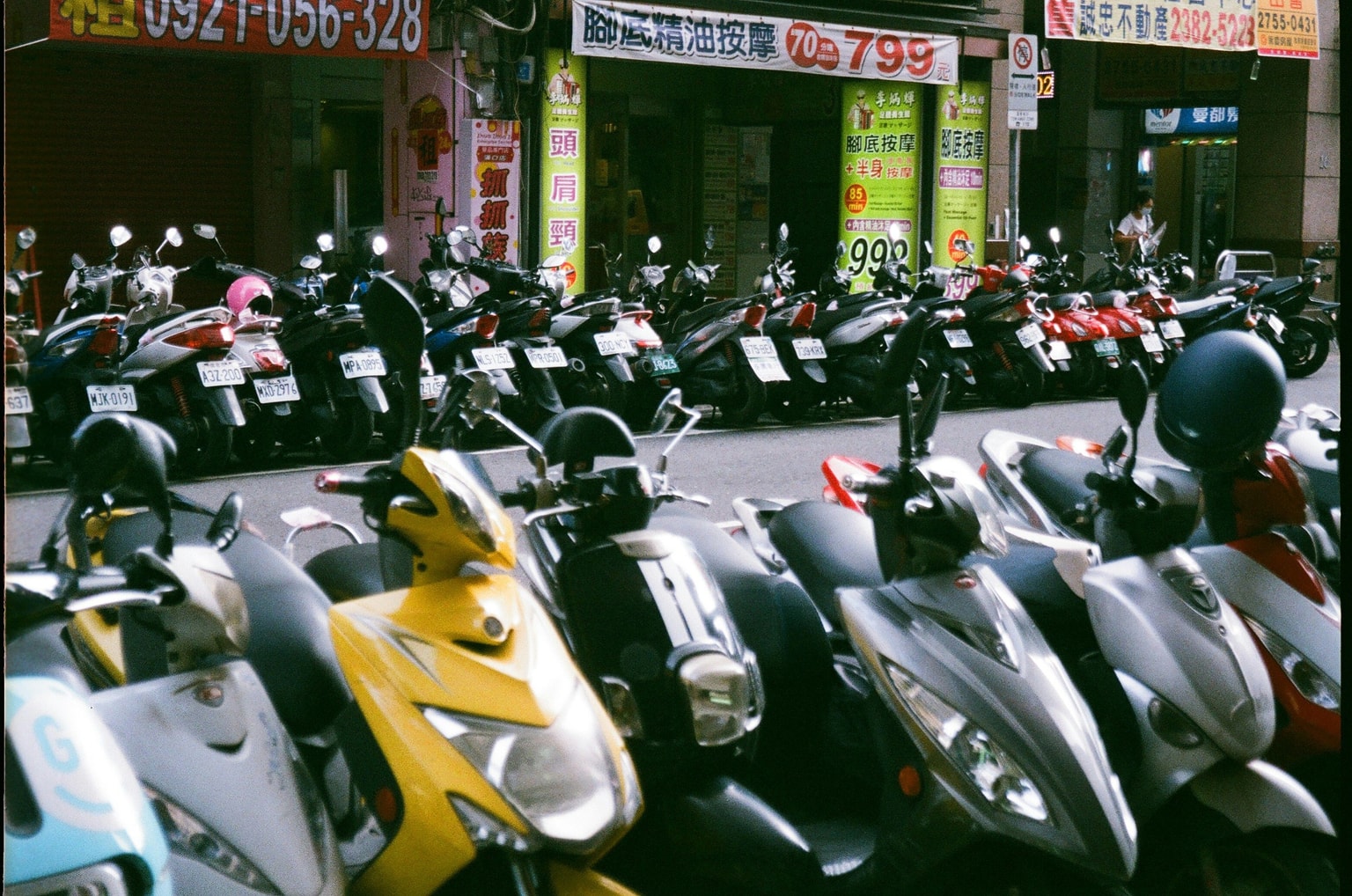Rows of parked scooters line a busy street in front of shops with colorful signage.