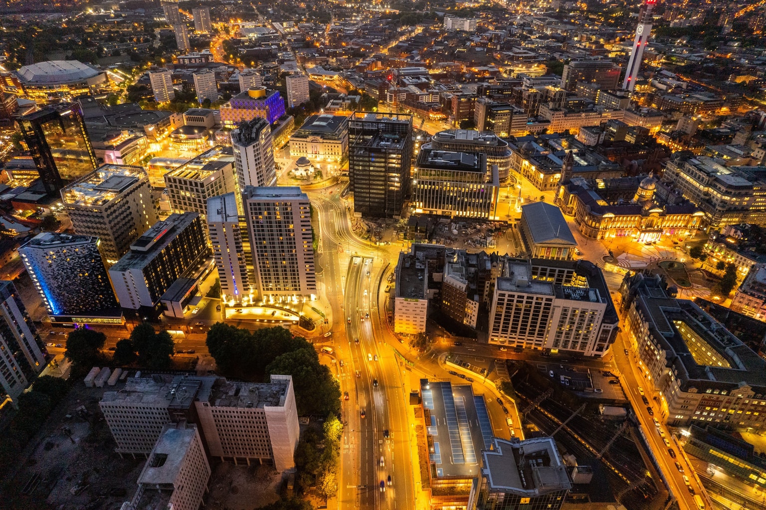 Aerial view of a Birmingham cityscape at night, with illuminated streets and buildings, showcasing a vibrant urban environment.