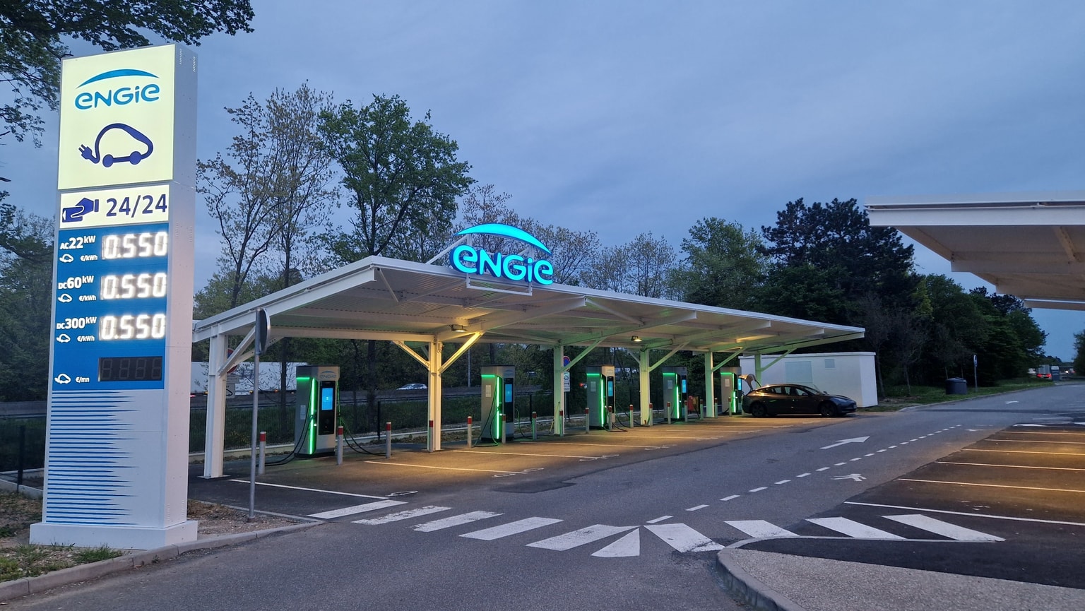 Station de recharge extérieure pour véhicules électriques avec plusieurs points de charge, entourée d'arbres et arborée d'une signalétique lumineuse « ENGIE ».