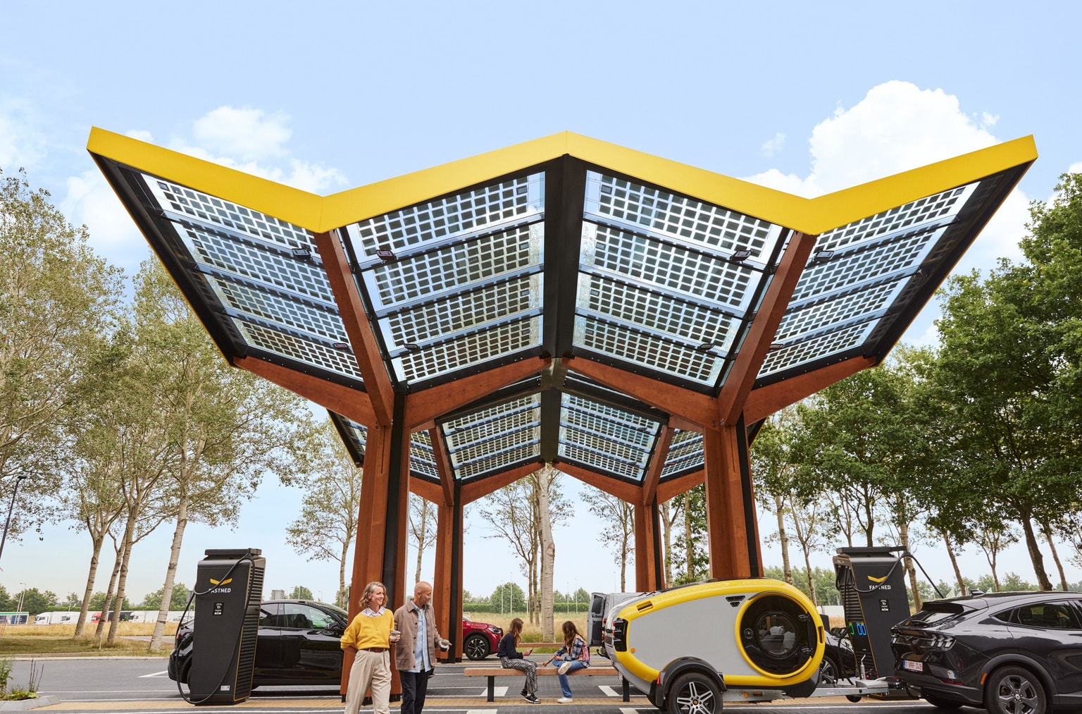 Station de recharge Fastned alimentée à l'énergie solaire, dotée d'un toit à l'architecture unique, pouvant accueillir plusieurs véhicules électriques et deux personnes passant en dessous.