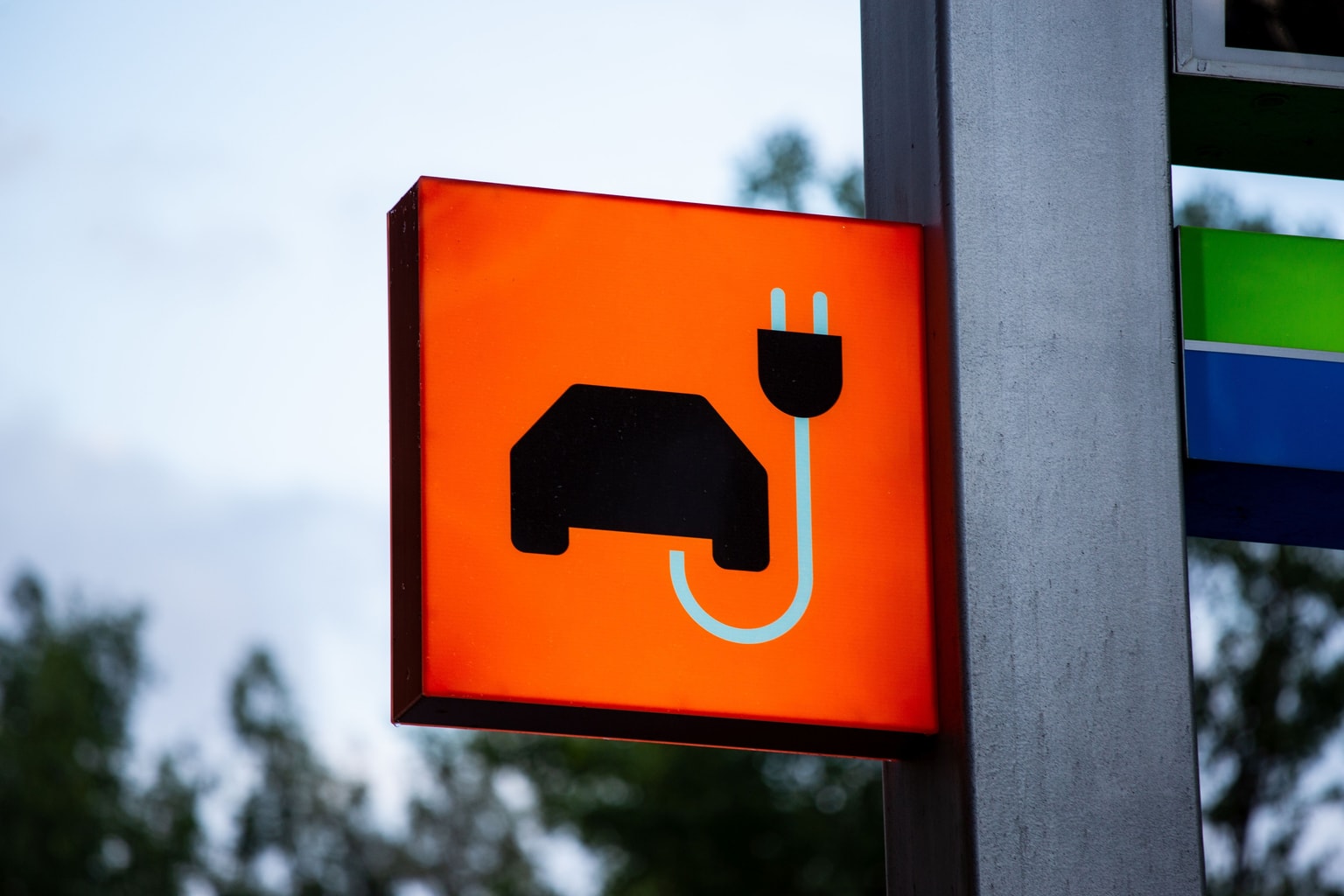 A sign with an icon of a car and a plug on an orange background, indicating an electric vehicle charging station.