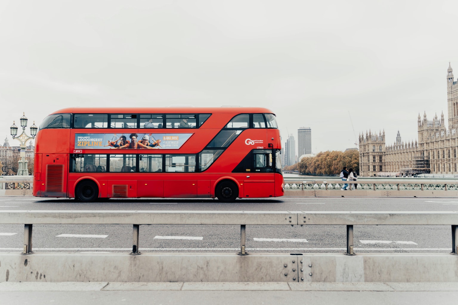Red double-decker bus on Westminster Bridge, London, with the Houses of Parliament in the background on an overcast day.