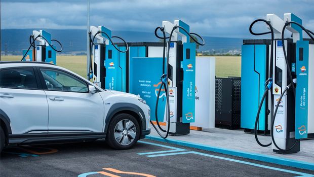 Carregamento de carro elétrico Repsol numa estação com várias unidades de carregamento azuis e brancas sob um céu nublado.