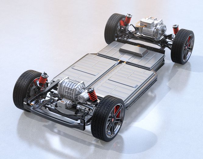 Electric vehicle chassis with visible battery pack, dual motors, suspension system, and wheels on a smooth, light-colored surface.